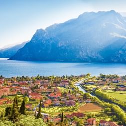 Panoramablick auf Torbole am Gardasee mit rotgedeckten Häusern, grünen Feldern und dramatischen Bergen am blauen See.