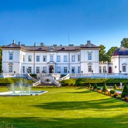 Weißer neoklassizistischer Tiskeviciai-Palast in Palanga mit gepflegten Gärten, Brunnen und symmetrischen Treppen unter blauem Himmel.