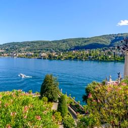 Verzierte Statue in blühenden Gärten auf Isola Bella mit Blick auf den Lago Maggiore mit Bergen und einem Boot auf blauem Wasser.
