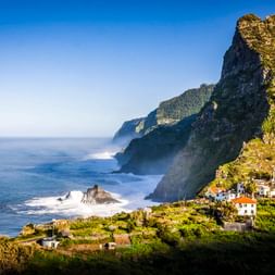 Dorf Boaventura an Madeiras Nordküste mit weißen Häusern auf grünen Terrassen unterhalb dramatischer Klippen und dem Atlantik.