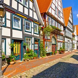 Bunte Fachwerkhäuser mit orangen Ziegeldächern säumen die Kopfsteinpflaster-Bäckerstraße in Rinteln. Straßenlaterne und Blumentöpfe schmücken die Straße.