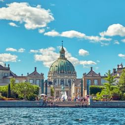 Blick über das Wasser auf Schloss Amalienborg in Kopenhagen mit der grünen Kupferkuppel der Frederikskirche hinter den symmetrischen Palastgebäuden.