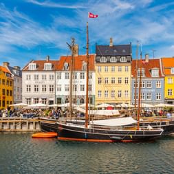 Historische Holzsegelschiffe im Nyhavn-Hafen mit bunten gelben, weißen und orangen Gebäuden entlang der Uferpromenade in Kopenhagen.
