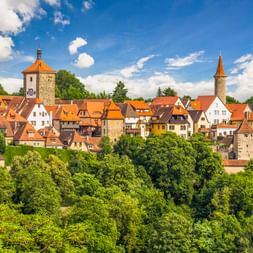 Historische Stadt Rothenburg ob der Tauber mit orangefarbenen Dächern, mittelalterlichen Türmen und Fachwerkhäusern, umgeben von grünen Bäumen.