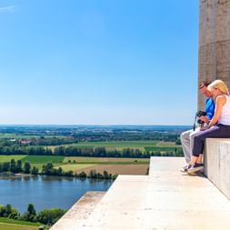 Zwei Personen sitzen auf der Steinterrasse der Walhalla bei Donaustauf und blicken auf die Donau und die grüne Tallandschaft.
