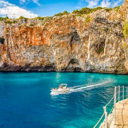 Türkisfarbene Wasserbucht bei der Grotta Zinzulusa nahe Castro mit Kalksteinfelsen, einem Boot und Steinstufen mit Metallgeländer.