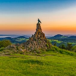 Steinernes Fliegerdenkmal mit Adlerskulptur auf der Wasserkuppe, Hessen. Grüne Hügellandschaft im Hintergrund unter Abendhimmel.