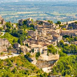 Les Baux-de-Provence, ein mittelalterliches Steindorf auf Felsklippen, umgeben von grüner Vegetation mit dem Provence-Tal darunter.