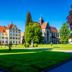 Kloster und Schloss Salem mit weißen Barockgebäuden, gotischer Kirche und gepflegten Rasenflächen unter blauem Himmel am Bodensee.