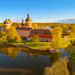 Luftaufnahme von Schloss Gripsholm in Mariefred, ein roter Backsteinpalast mit Kuppeltürmen auf einer kleinen Insel umgeben von Wasser und Bäumen.