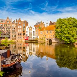 Traditionelle niederländische Grachten in Delfshaven, Rotterdam, spiegeln sich im ruhigen Wasser. Historische Boote liegen am Kanal mit grünen Bäumen.