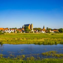 Panoramablick auf Verden mit Kirchtürmen und traditionellen Häusern über grüne Wiesen und die Weser unter klarem blauen Himmel.