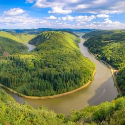 Panoramablick auf die Saarschleife bei Mettlach mit einer markanten Flussschleife der Saar, umgeben von bewaldeten Hügeln.