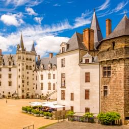 Château des Ducs de Bretagne in Nantes mit weißen Steinmauern, rundem Turm und Innenhof mit Marktständen unter blauem Himmel.