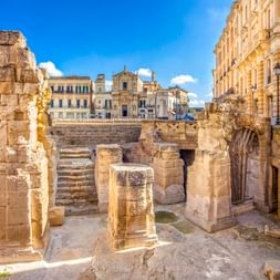 Ruinen des antiken römischen Amphitheaters an der Piazza Sant'Oronzo in Lecce mit Steinsäulen, Bögen und Stufen, umgeben von historischen Gebäuden.