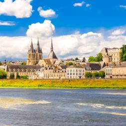 Blick auf Blois über die Loire mit historischen Gebäuden und Kirchtürmen unter blauem Himmel mit weißen Wolken.
