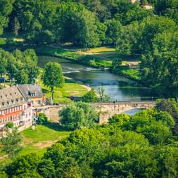 Luftaufnahme von Echternach mit einer Steinbrücke über einen Fluss, umgeben von üppigen grünen Bäumen und historischen Gebäuden mit orangen Dächern.