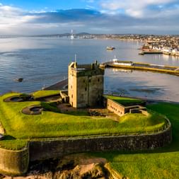 Luftaufnahme von Broughty Castle auf grüner Wiese am Firth of Tay. Die Steinfestung überblickt ruhige Gewässer mit Dundee im Hintergrund.