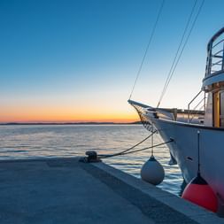 Weißes Boot Carpe Diem an einem Pier bei Sonnenuntergang. Der Himmel zeigt orange und blaue Farbtöne, ruhiges Wasser reflektiert das Abendlicht.