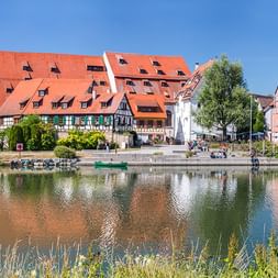 Historische Stadt Rottenburg am Neckar mit bunten Fachwerkhäusern und roten Dächern, die sich im Neckar unter blauem Himmel spiegeln.