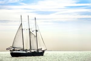 Traditionelles Segelschiff Mare fan Fryslan mit dunklem Rumpf und drei weißen Segeln auf ruhigem Wasser unter bewölktem Himmel.