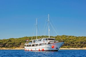 Weiße Motoryacht MS Azimut mit zwei Masten und roten Fendern vor Anker auf ruhigem blauen Wasser, mit grüner bewaldeter Küste im Hintergrund.