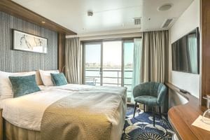 Moderne Kabine auf der MS Swiss Crown mit Doppelbett, türkisfarbenen Kissen, Sessel, TV und großen Fenstern mit Flussblick.