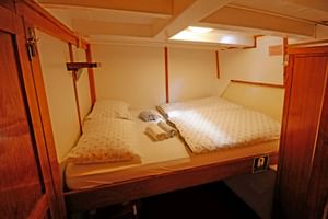 Kompakte Doppelkabine auf der MS Orkan mit zwei Etagenbetten, weißer Bettwäsche, Holzverkleidung und einem Schrank. Handtücher liegen auf jedem Bett.