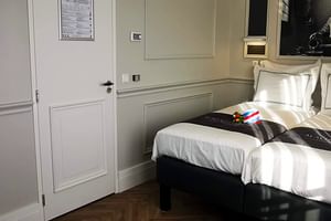 Modernes Suite-Schlafzimmer auf der MS Magnifique IV mit Doppelbett, weißer Bettwäsche, Holzboden, getäfelten Wänden und Kunstwerk über dem Kopfteil.