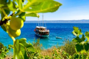 MS Aneta, ein hölzernes Segelschiff, ankert in kristallklarem türkisfarbenem Wasser. Blick eingerahmt von Zitronenbaumzweigen.