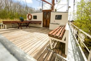 Holzdeck des Dreimastklippers Elizabeth mit Holzbänken, Kabineneingang und Takelage. Bäume im Hintergrund sichtbar.