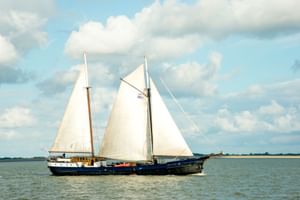 Traditionelles niederländisches Segelschiff Wapen fan Fryslân mit dunkelblauem Rumpf und weißen Segeln auf ruhigem Wasser unter bewölktem Himmel.