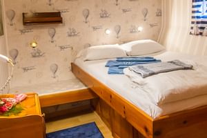Gemütliche Kabine auf der MS Panagiota mit Doppelbett, weißen Kissen, maritimer Tapete, Holzmöbeln, Spiegel und Fenster mit weißen Vorhängen.