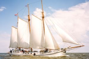 Dreimastklipper Elizabeth segelt mit weißen Segeln vor blauem Himmel mit Wolken. Das weiße Schiff bewegt sich durch ruhiges Wasser.