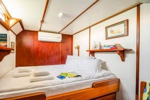 Kompakte Kabine auf der MS Caprice mit zwei Einzelbetten, weißer Bettwäsche, Holzverkleidung, Klimaanlage, Regal mit Büchern und gerahmten Bildern.