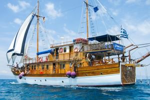 MS Panagiota, ein hölzernes Segelschiff mit weißem Rumpf und zwei Masten, segelt auf blauem Meer unter klarem Himmel mit griechischer Flagge.