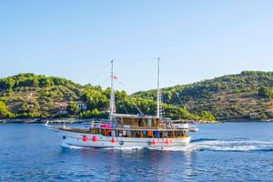 Motorschiff MS Dalmatino mit roten Fendern auf ruhigem blauen Wasser. Grüne terrassierte Hügel mit vereinzelten Gebäuden im Hintergrund.