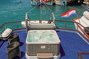 Whirlpool auf dem Sonnendeck der MS Azimut mit blauem Teppich, Korbstühlen und kroatischer Flagge. Türkisfarbenes Wasser und Boote im Hintergrund.