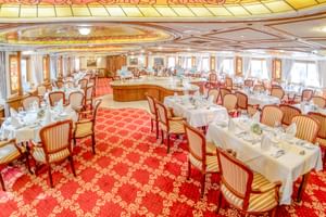 Elegantes Restaurant an Bord der MS Prinzessin Katharina mit weiß gedeckten Tischen, gestreiften Polsterstühlen, rotem Teppich und Decke.