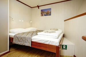 Saubere Kabine auf der MS Aria mit Doppelbett, beigen Wänden, Holzboden und gefalteten Handtüchern. Ein Bild mit Segelbooten hängt über dem Bett.