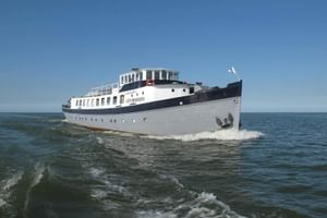 Weiß-dunkelblaues Passagierschiff Floor van Aemstel fährt auf offenem Wasser unter klarem blauen Himmel und erzeugt eine Bugwelle.