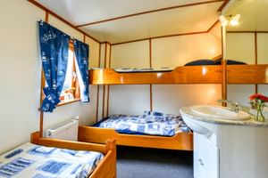 Kabine auf Klipper Elizabeth mit Etagenbett, Einzelbett, Waschbecken und maritimen blauen Vorhängen. Holzvertäfelte Wände und Bettwäsche mit blauen Mustern.