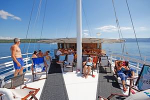 Passagiere entspannen auf Sonnenliegen auf dem Oberdeck der MS Kazimir. Das Deck verfügt über einen überdachten Essbereich und Mast, blaues Wasser ist sichtbar.
