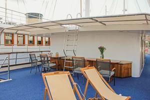 Sonnendeck der MS Azimut mit beigen Liegestühlen auf blauem Teppich, überdachtem Sitzbereich mit Holzmöbeln und weißem Sonnensegel.