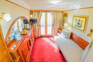 Oberdeck-Kabine auf der MS Prinzessin Katharina mit zwei Einzelbetten, rotem Teppich, Holzmöbeln, Spiegel und Balkontür mit beigen Vorhängen.