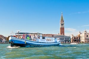 Blaues Kreuzfahrtschiff MS Vita Pugna in der Lagune von Venedig mit Markusturm und historischen Gebäuden im Hintergrund.