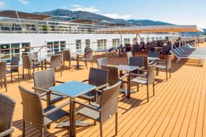 Sonnendeck der MS Prinzessin Katharina mit Holzboden, Rattanmöbeln, gestreiften Liegestühlen und Bergblick unter blauem Himmel.
