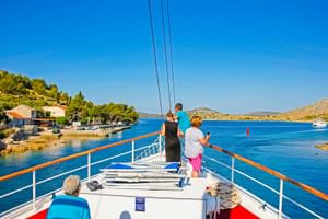 Blick vom Sonnendeck der MS Sveti Vid mit Passagieren, die die kroatische Küste mit blauem Wasser, Küstendorf und Hügeln genießen.
