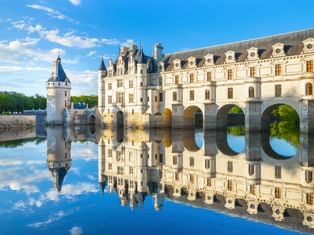 Schloss Chenonceau im Loiretal mit weißer Renaissance-Fassade und Bogenbrücke über ruhigem Wasser, perfekte Spiegelung unter blauem Himmel.