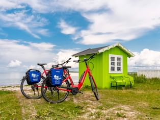 Zwei Fahrräder mit blauen Taschen neben einem leuchtend grünen Strandhaus mit weißen Fenstern in Ærøskøbing, Dänemark. Meer und blauer Himmel.